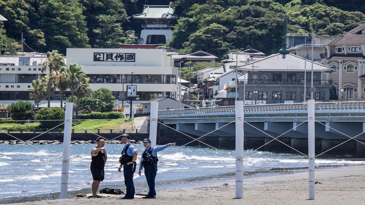 Police officers ask a man to evacuate an empty beach due to a tsunami warning in Fujisawa city (Photo-AFP)