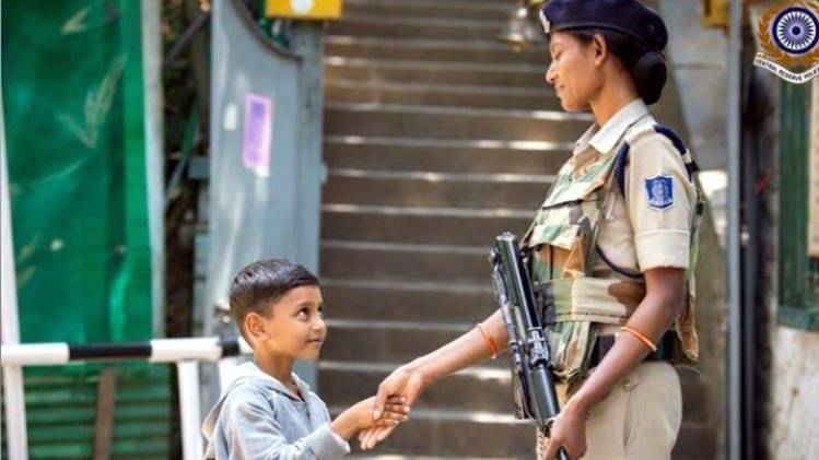 श्रीनगर में महिला सुरक्षाकर्मी से हाथ मिलाता बच्चा (फोटो-IANS)