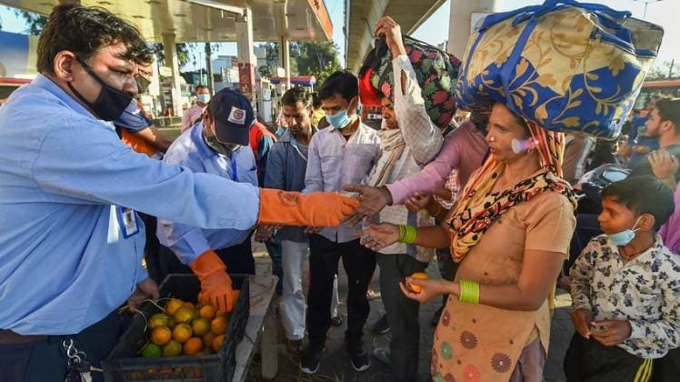 दिल्ली में मजदूरों के बीच फल बांटते लोग (फोटो- पीटीआई)