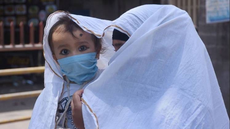 सूरत में एक महिला अपने बच्चे के साथ खुद को ढकती हुई (फोटो- पीटीआई)