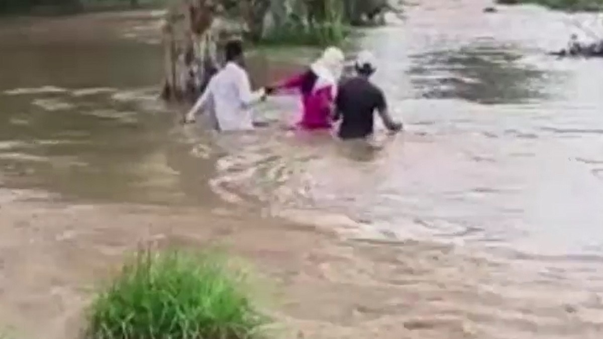 दो ग्रामीणों की मदद से नदी पार करती टीचर.