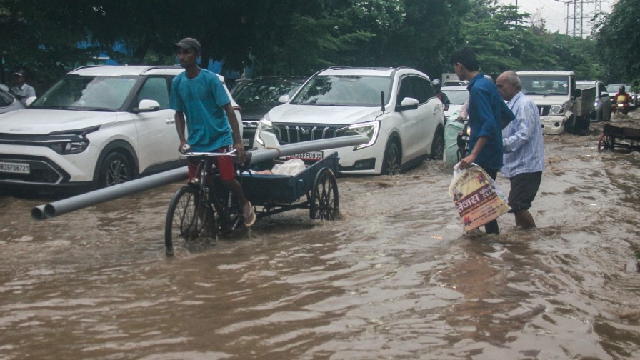 Commuters wade through a waterlogged road heavy rainfall, in Gurugram July 31, 2025. (PTI Photo)