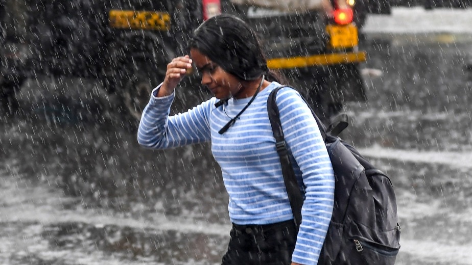 A commuter crosses a road during rain, in Mumbai (PTI Photo)