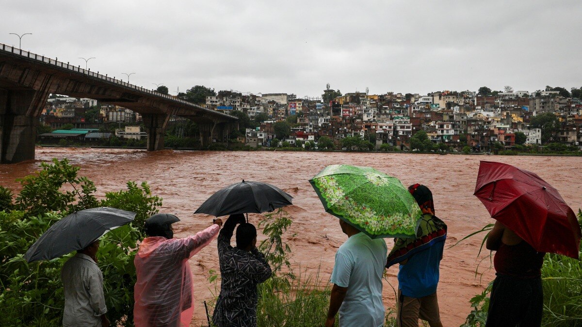जम्मू में 26 अगस्त, 2025 को लोग भारी बारिश के बीच उफनती तवी नदी को देखते हुए. (Photo: PTI)