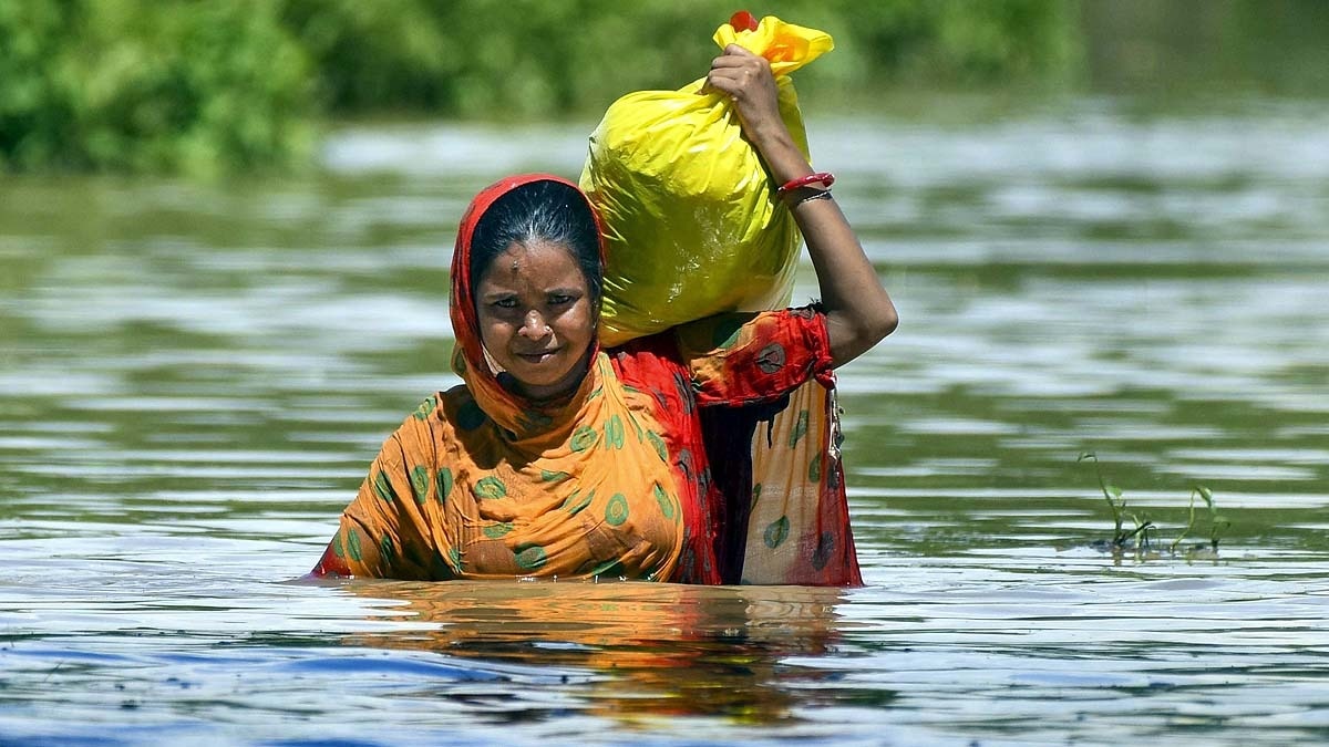 असम के होजाई जिले की जरानी गांव में बाढ़ग्रस्त इलाके को पार करती हुई एक महिला, जिसके घर का ज्यादातर सामान बह गया. (File Photo: PTI)