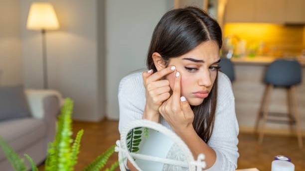 Portrait of beautiful young woman squeezing pimples while looking at the mirror. Pimple on cheek. Young woman squeeze her acne in front of the mirror. I'm sure this will go away if I pop it.