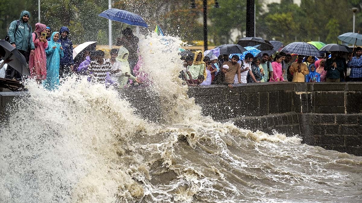मुंबई के गेटवे ऑफ इंडिया के पास बारिश के बीच उफनते लहरों को देखते लोग. (Photo: PTI)