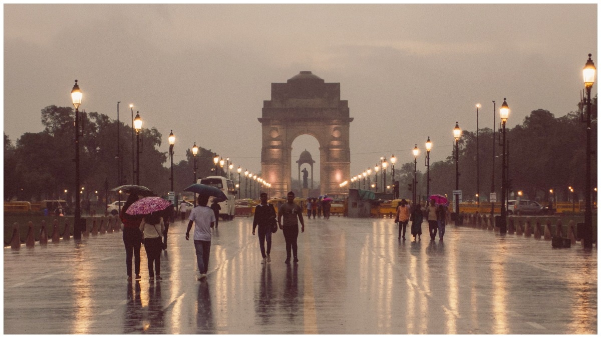 Moody evening scene at India Gate with reflections on the wet road and people walking.