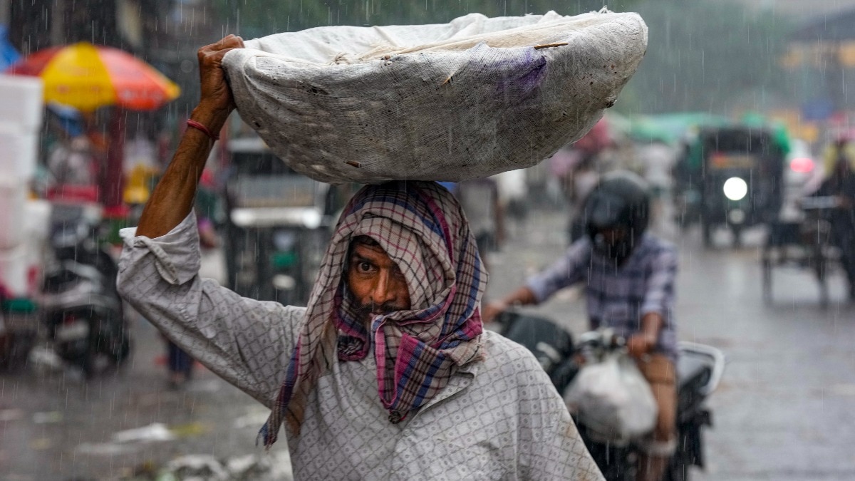 नई दिल्ली की आजादपुर मंडी में जलभराव के बीच सड़क पार करता एक दुकानदार.(Photo- PTI)