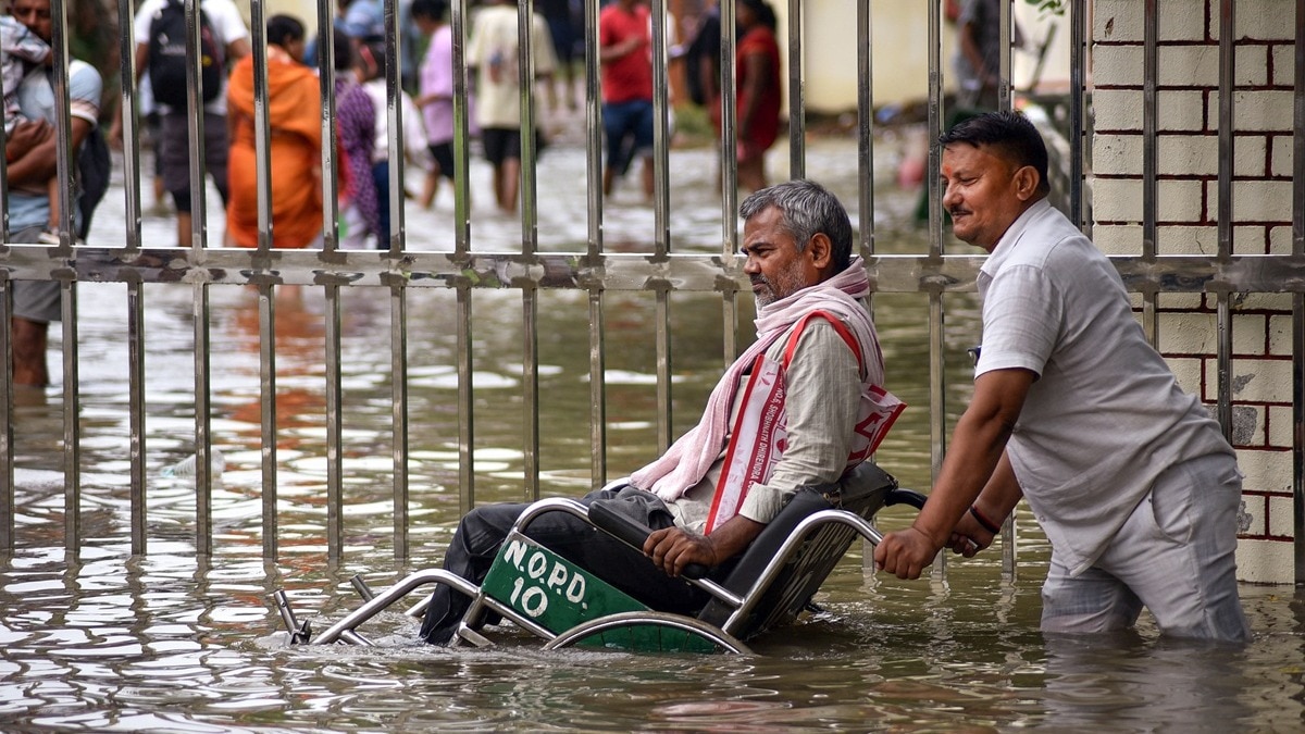 वाराणसी: BHU अस्पताल के पास बारिश के पानी में दिव्यांग की मदद करता एक शख्स.(Photo:PTI)