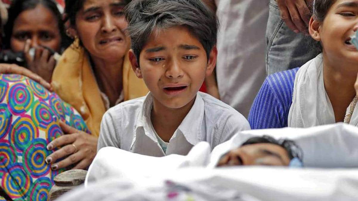 दिल्ली हिंसा में मारे गए पिता के अर्थी पर रोता बेटा (फोटो- Reuters)