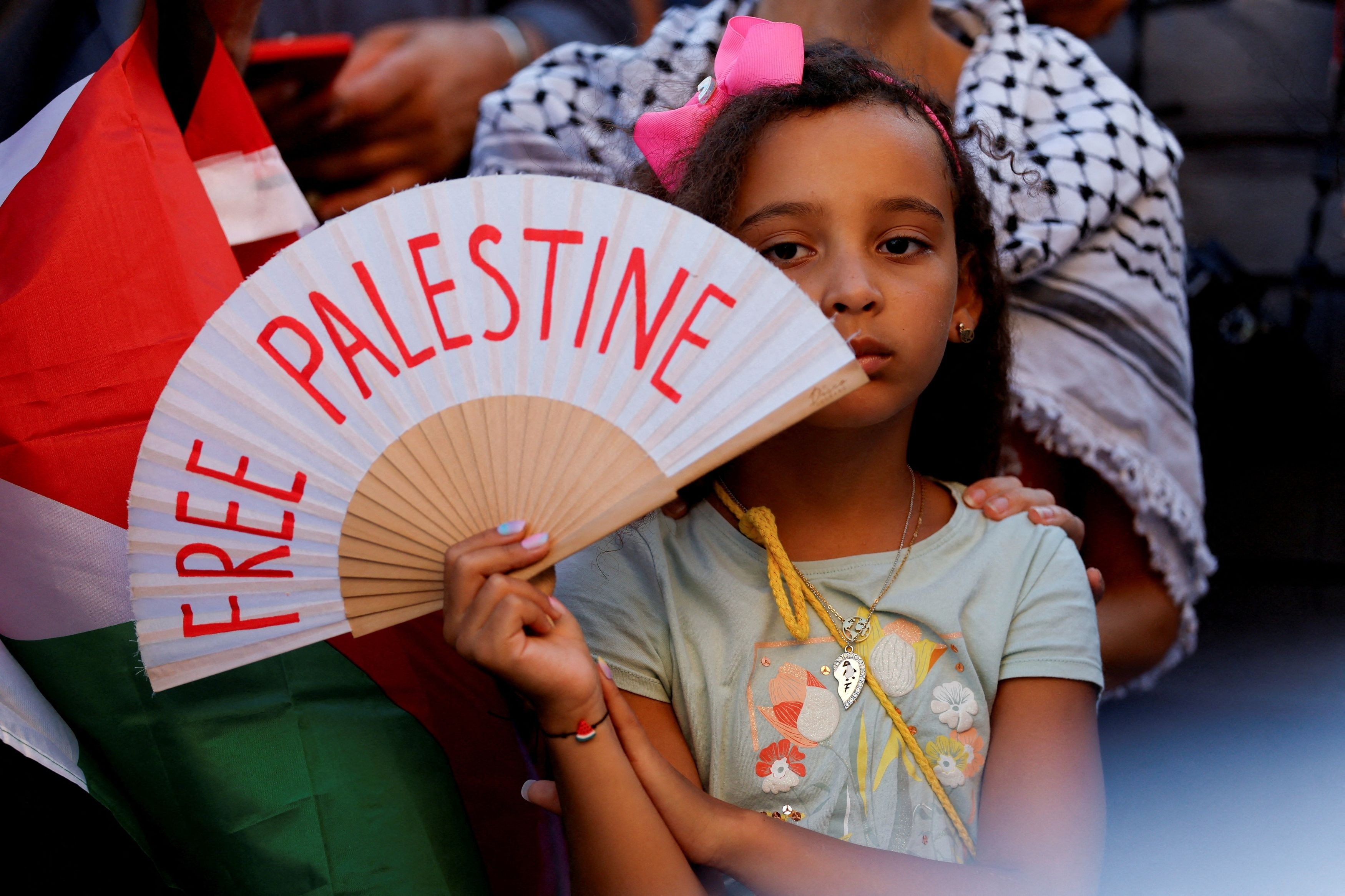 A girl holds a hand fan reading 'Free Palestine'