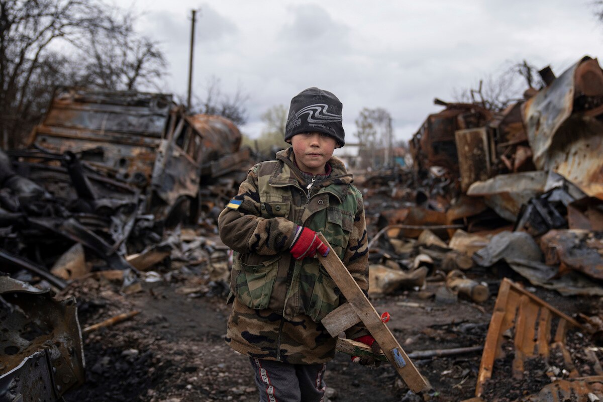 Yehor, 7, holds a toy rifle next to destroyed Russian military vehicles near Chernihiv, Ukraine.