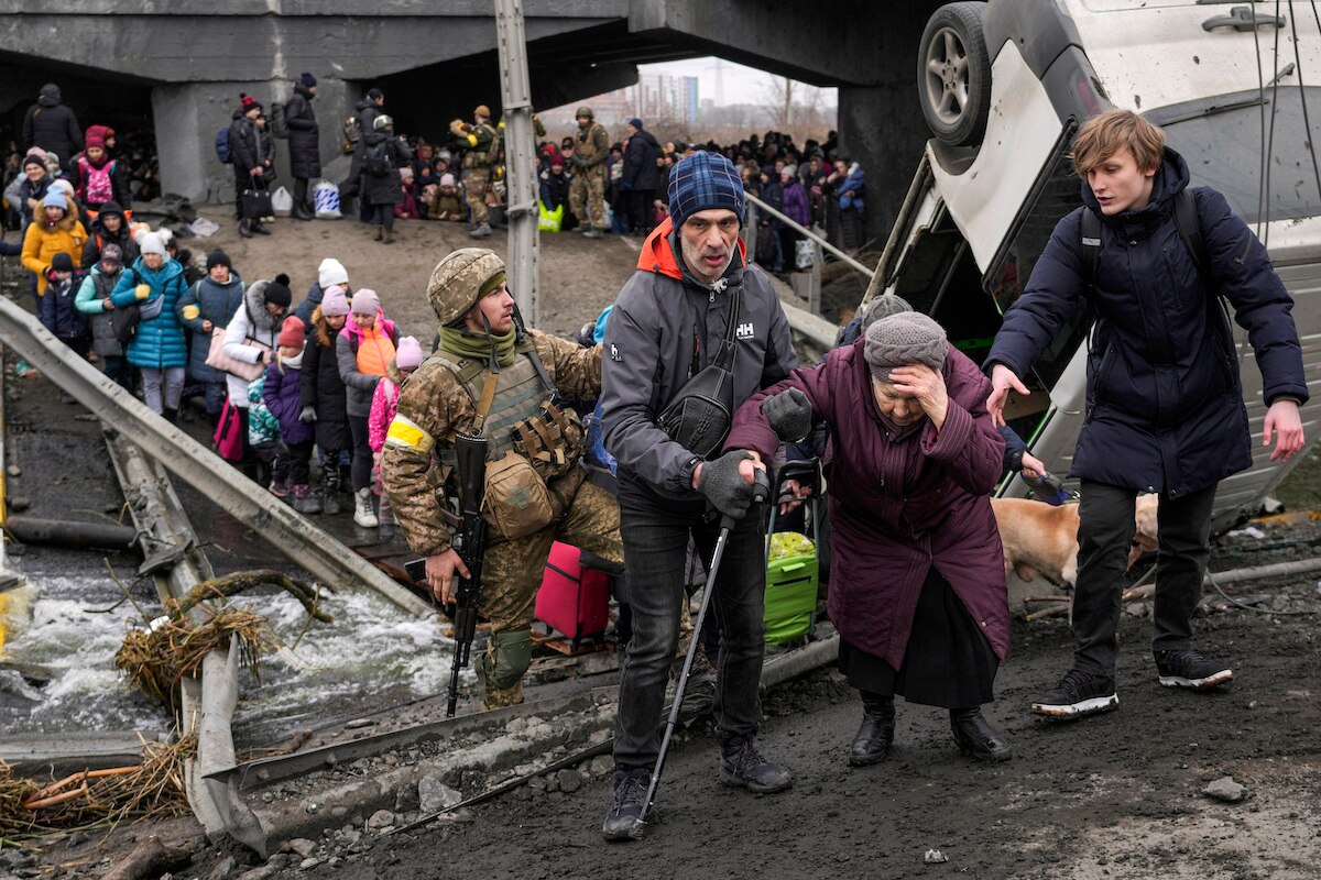 An elderly woman is assisted to cross the Irpin River on an improvised path under a bridge that was destroyed by Ukrainian troops to slow the Russian military advance while fleeing the town of Irpin, Ukraine.