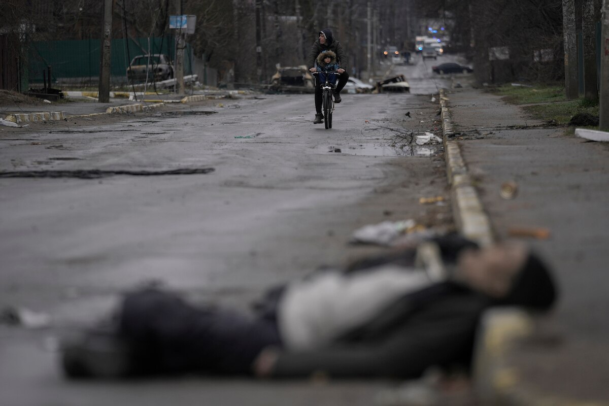 A man and child ride a bicycle through a street where civilian's bodies lie in the formerly Russian-occupied Kyiv suburb of Bucha, Ukraine.