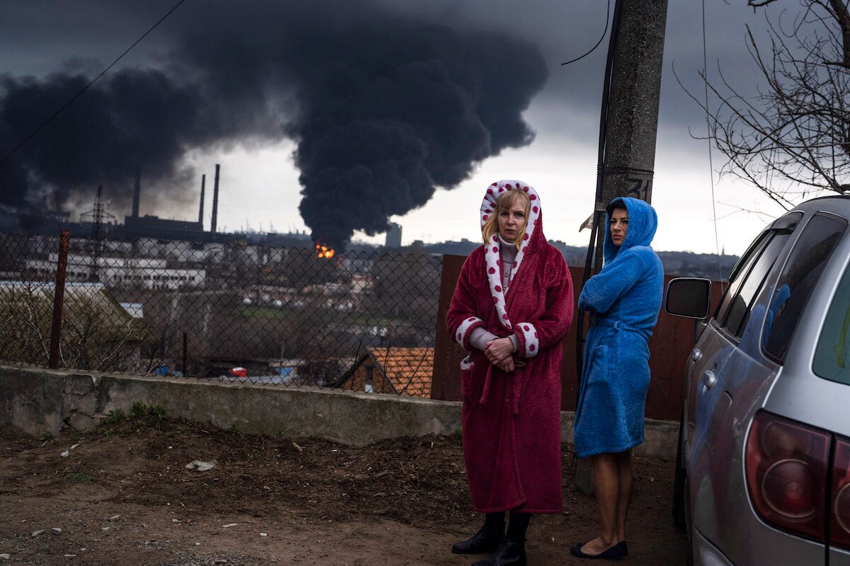 Women stand in their robes as smoke rises in the background after shelling in Odesa, Ukraine.