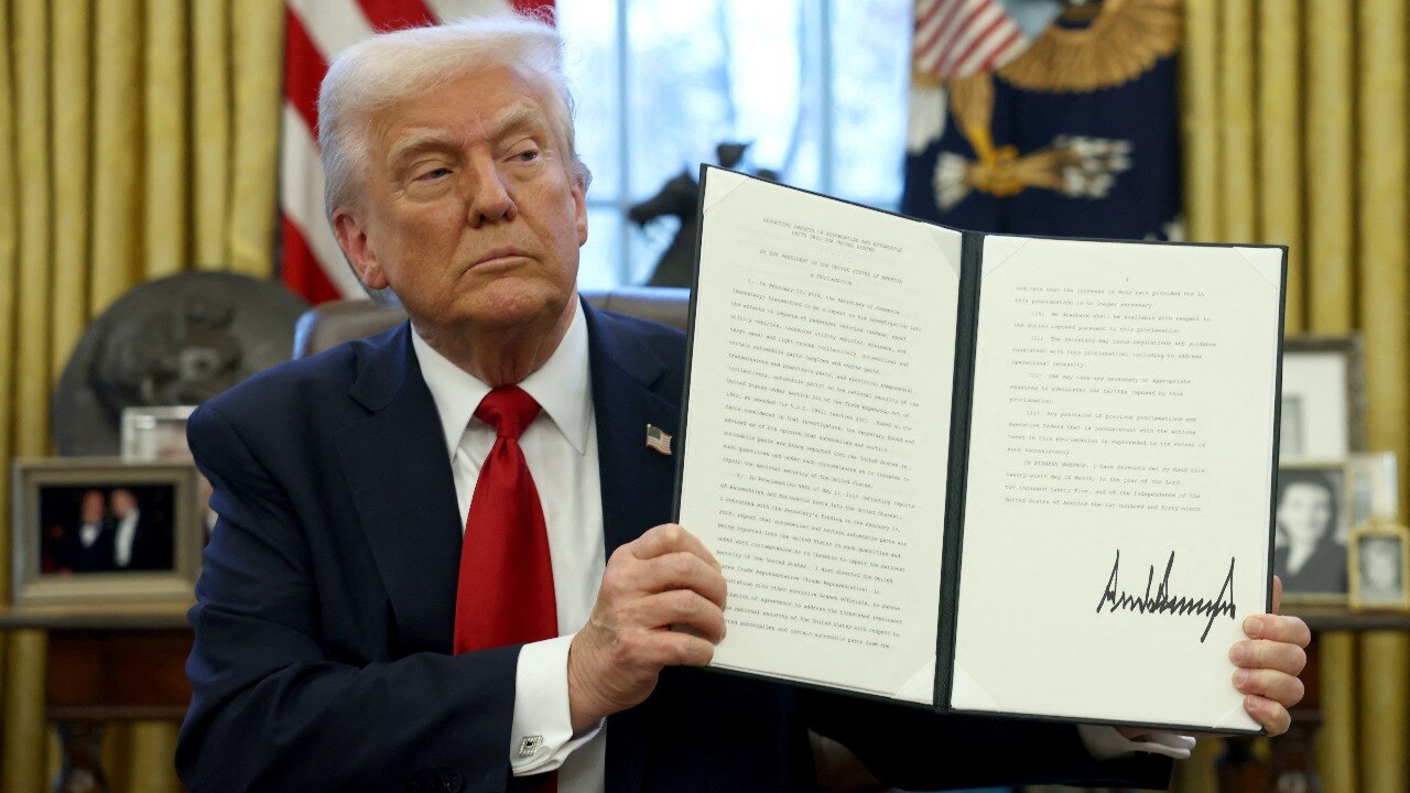 US President Donald Trump shows a signed document in the Oval Office at the White House. US President Donald Trump shows a signed document in the Oval Office at the White House.