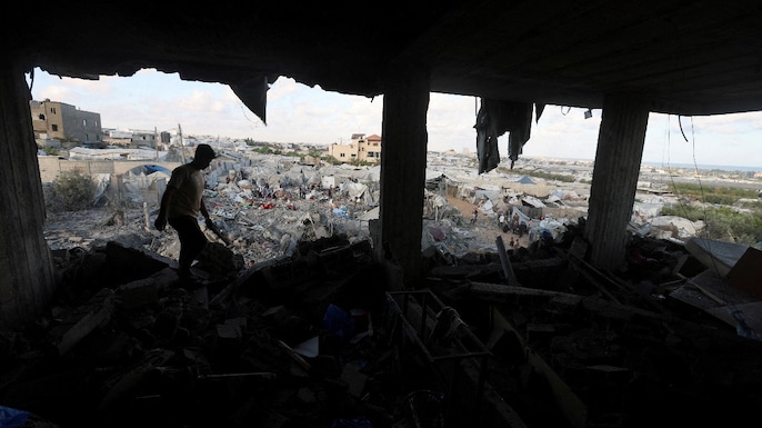 A Palestinian man inspects the site of an Israeli strike on a house whose residents were warned to evacuate before the attack, near a tent camp sheltering displaced people that was damaged in the strike