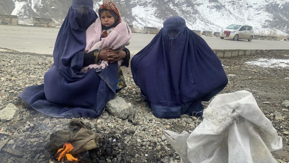 Women, toddler sitting in front of bonfire to keep themselves warm