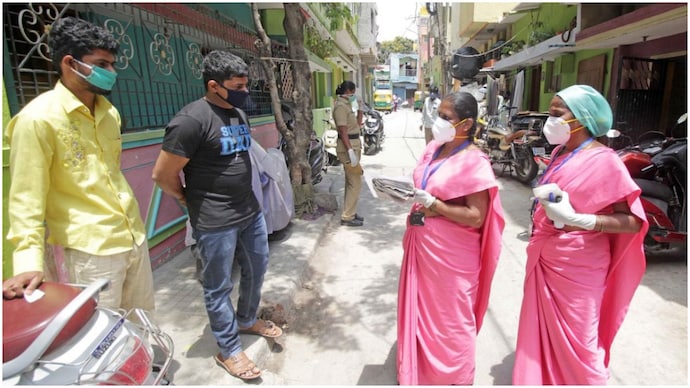 Asha workers in pink sarees seen talking to two men on a road