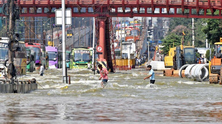 People use a cable to cross a waterlogged road following torrential rains in Bengaluru. People use a cable to cross a waterlogged road following torrential rains in Bengaluru.