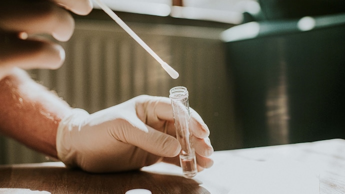 The spit test assesses 130 genetic variants that determine the risk score of prostate cancer. (Photo: Getty Image) Wearing latex gloves, one hand holds a small clear tube and immerses a cotton swab in the liquid. Location for copy.