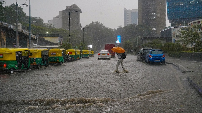 A pedestrian with an umbrella crosses a waterlogged road in Bengaluru. (Photo: PTI) Bengaluru rain broke record: What was behind the storm and will it happen again?