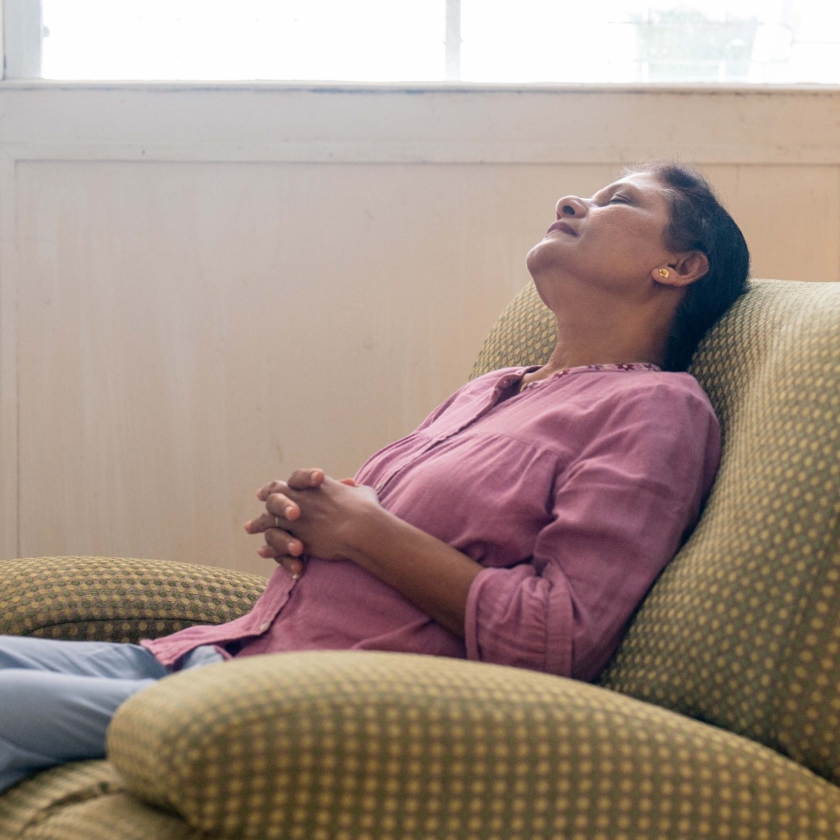 An elderly Asian woman is snoozing on a comfortable sofa in the living room, relaxing and recharging her energy while thinking pleasant thoughts and doing breathing exercises for harmony and balance.
