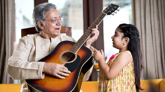 Elderly man holding guitar and playing with granddaughter at home