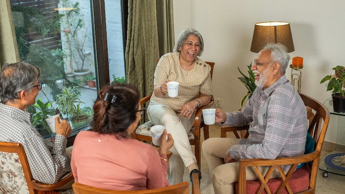 High angle view of senior friends talking and laughing cheerfully while having tea on chairs at home during weekend High angle view of senior friends talking and laughing cheerfully while having tea on chairs at home during weekend