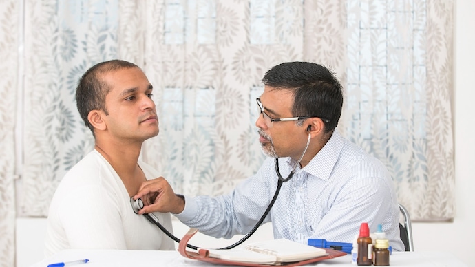 Mature Doctor examining a young patient at his clinic. The doctor is checking his heartbeat with a stethoscope.