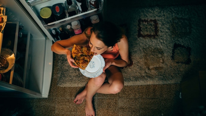 Woman eating in front of the refrigerator in the kitchen late night