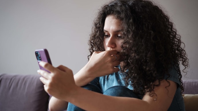 Worried anxious gen z girl looking at smartphone screen feeling upset scrolling on social media. Doomscrolling and mental health. Sad girl using mobile phone biting nails
