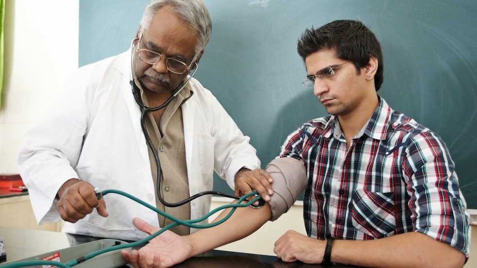 Doctor taking young adult's blood pressure