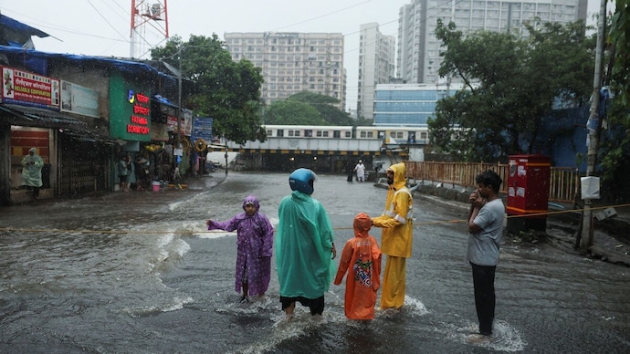 A municipal employee in a yellow raincoat stops people from crossing a flooded underpass after heavy rains in Mumbai. (Image: Reuters) mumbai monsoon weather flu like symptoms killer disease leptospirosis waterlogging sickness sick outbreak