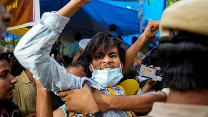 Security personnel detain a supporter of the Cockroach Janata Party (CJP) at Jantar Mantar in New Delhi. (Image: PTI) cockroach janta party protest cjp chalo sansad march dharmendra pradhan resignation union education minister resigns neet ug paper leak fir against students passport education abroad