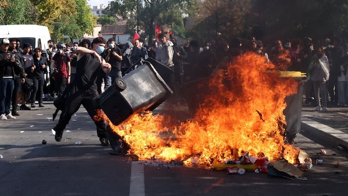 A masked protester throws a garbage bin into a fire set up by high school and university students in a street.