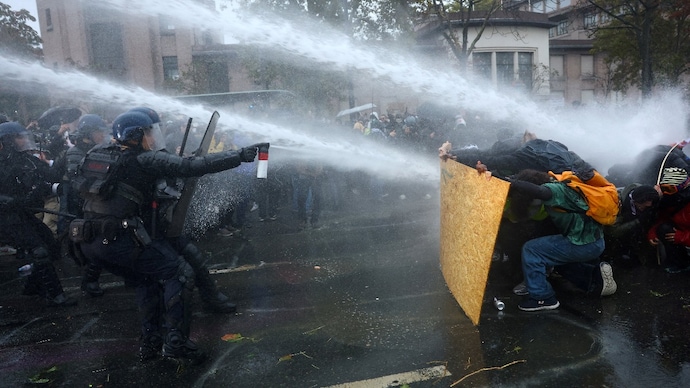 Protesters take cover behind a plywood board as French riot police and gendarmes use a water canon. (Photo- Reuters)