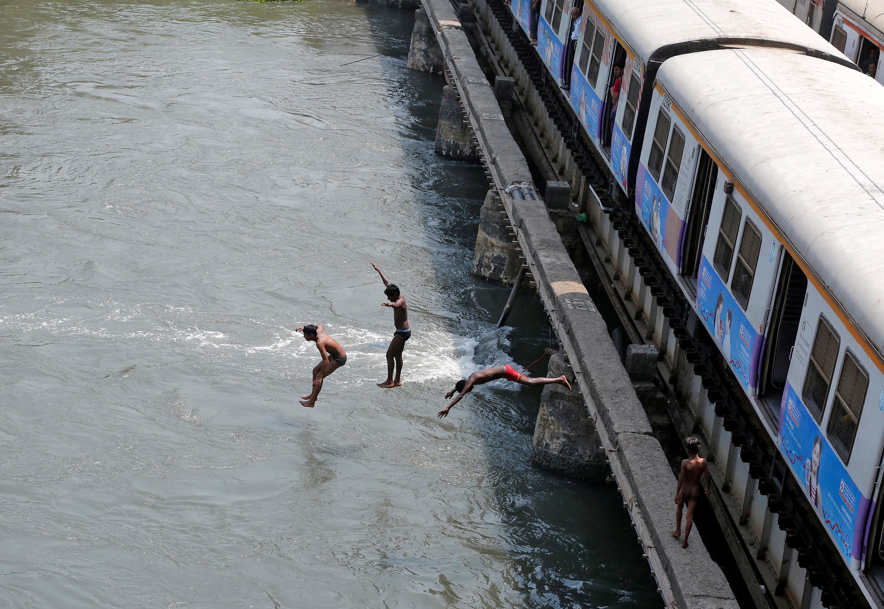 Boys jump from a railway bridge in a creek to cool off in Mumbai, India. (Photo: Reuters)