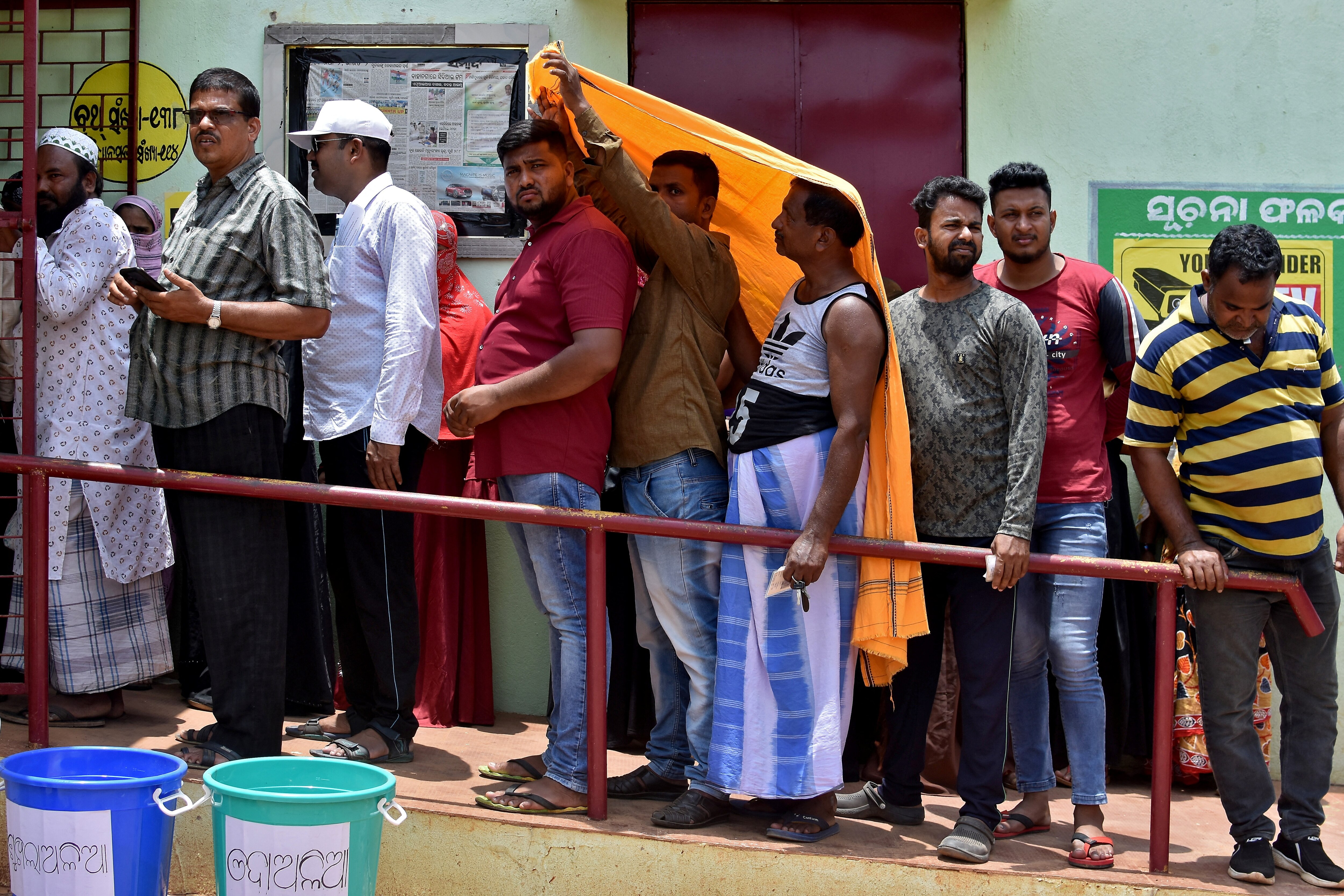 Men use a stole to cover from heat as they wait in a line outside a polling station to cast their votes. (Photo: Reuters)
