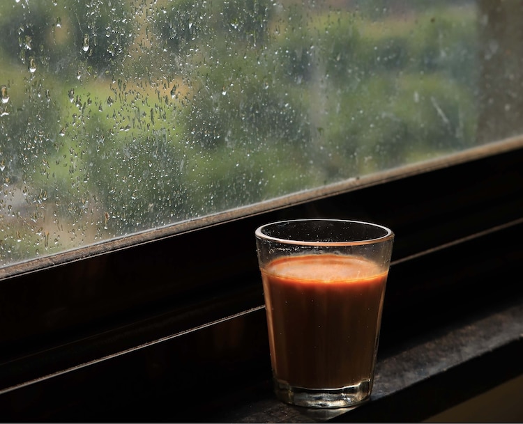 A glass of chai sits beside a window as it rains outside. (Photo: Getty)