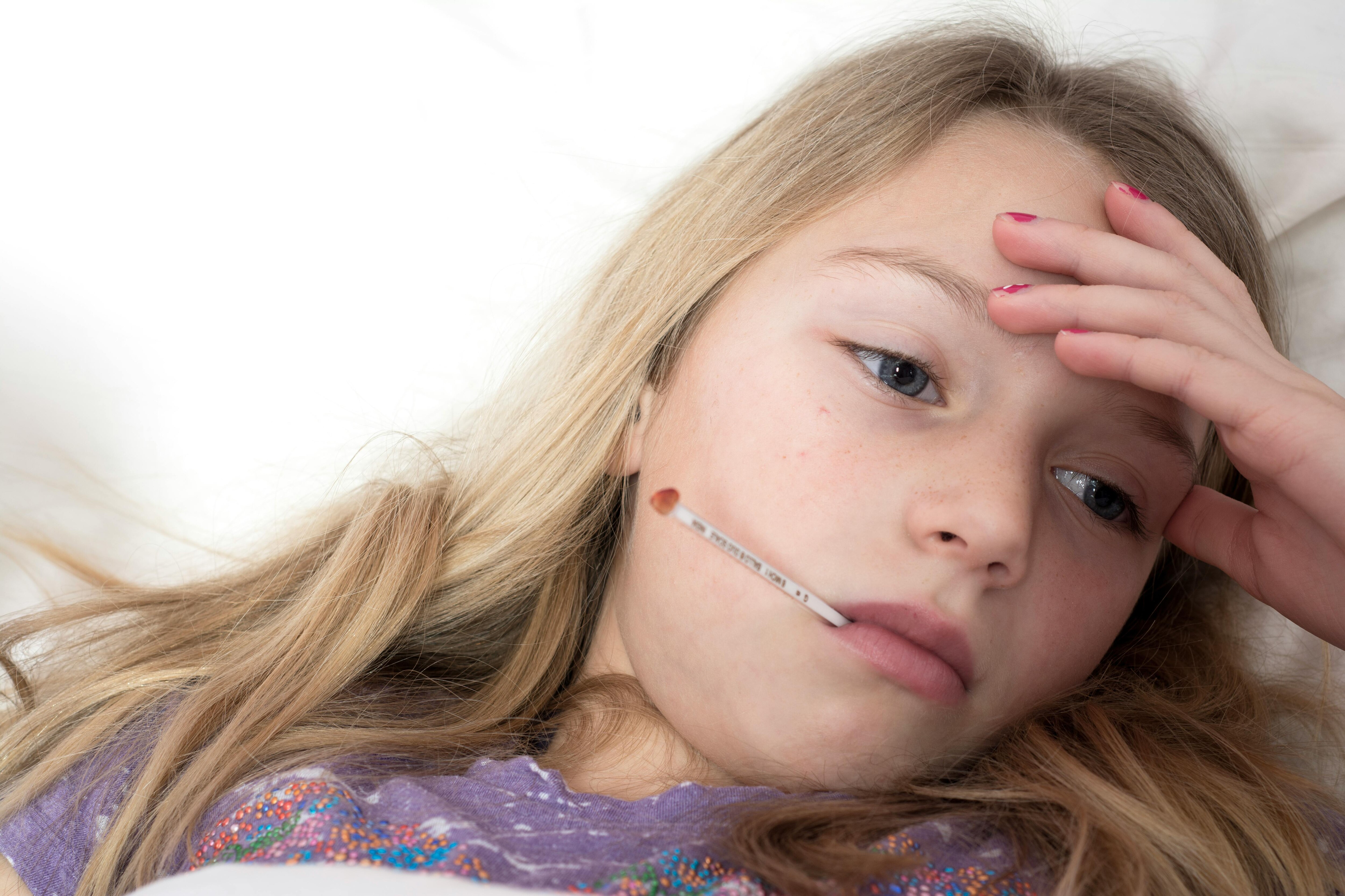  A young girl rests in bed with a thermometer, illustrating signs of illness and fatigue. (Photo: Pexels)