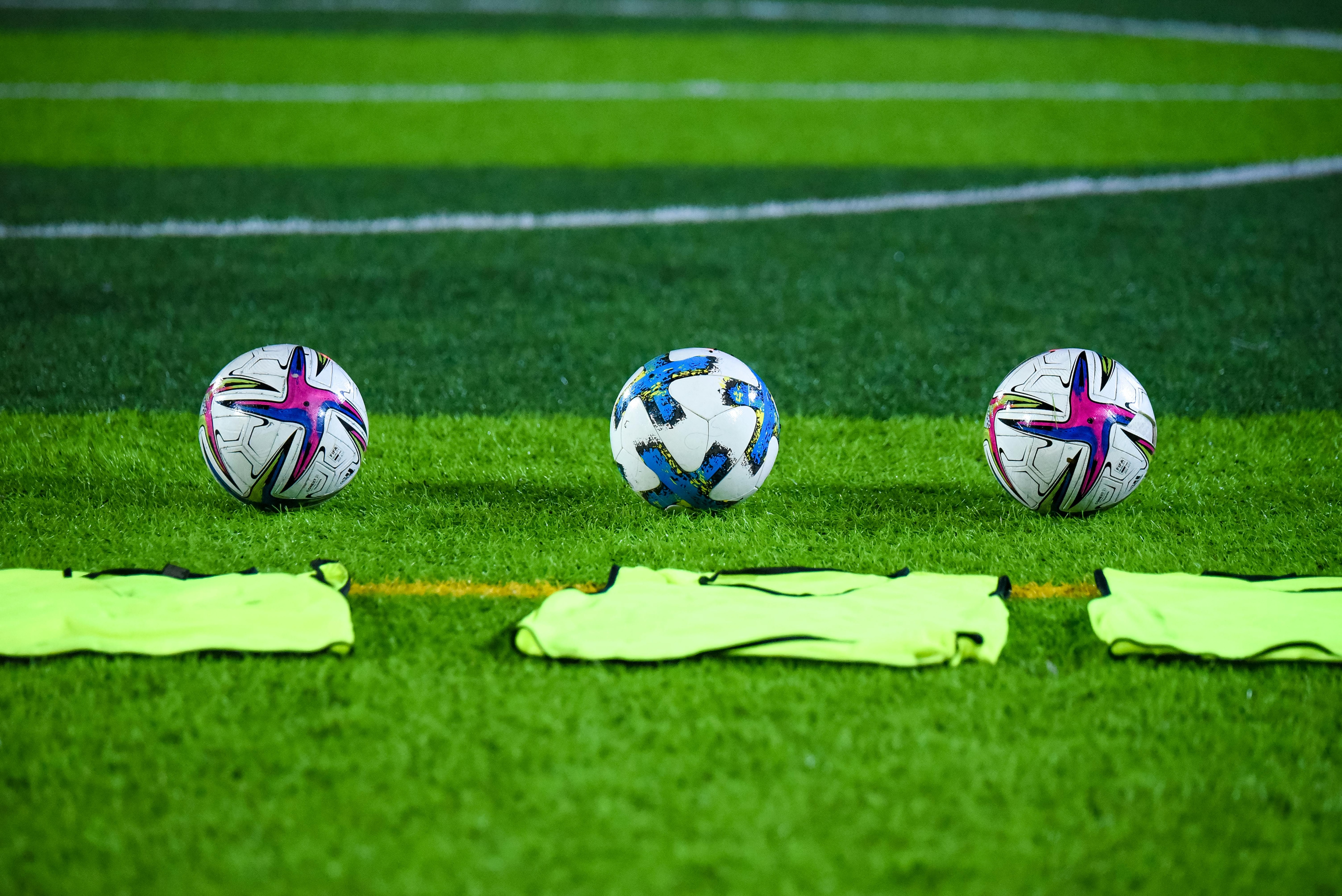 Three soccer balls and training bibs on a lush green field. (Photo: Pexels)