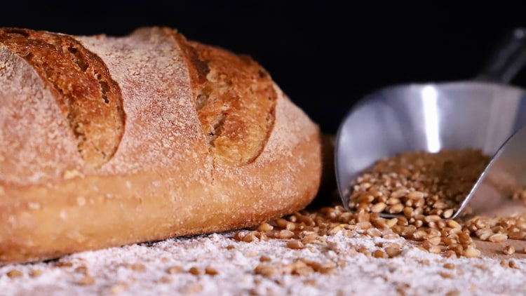 An image of a loaf of bread on a rustic surface with scattered wheat grains. (Photo: Pexels)