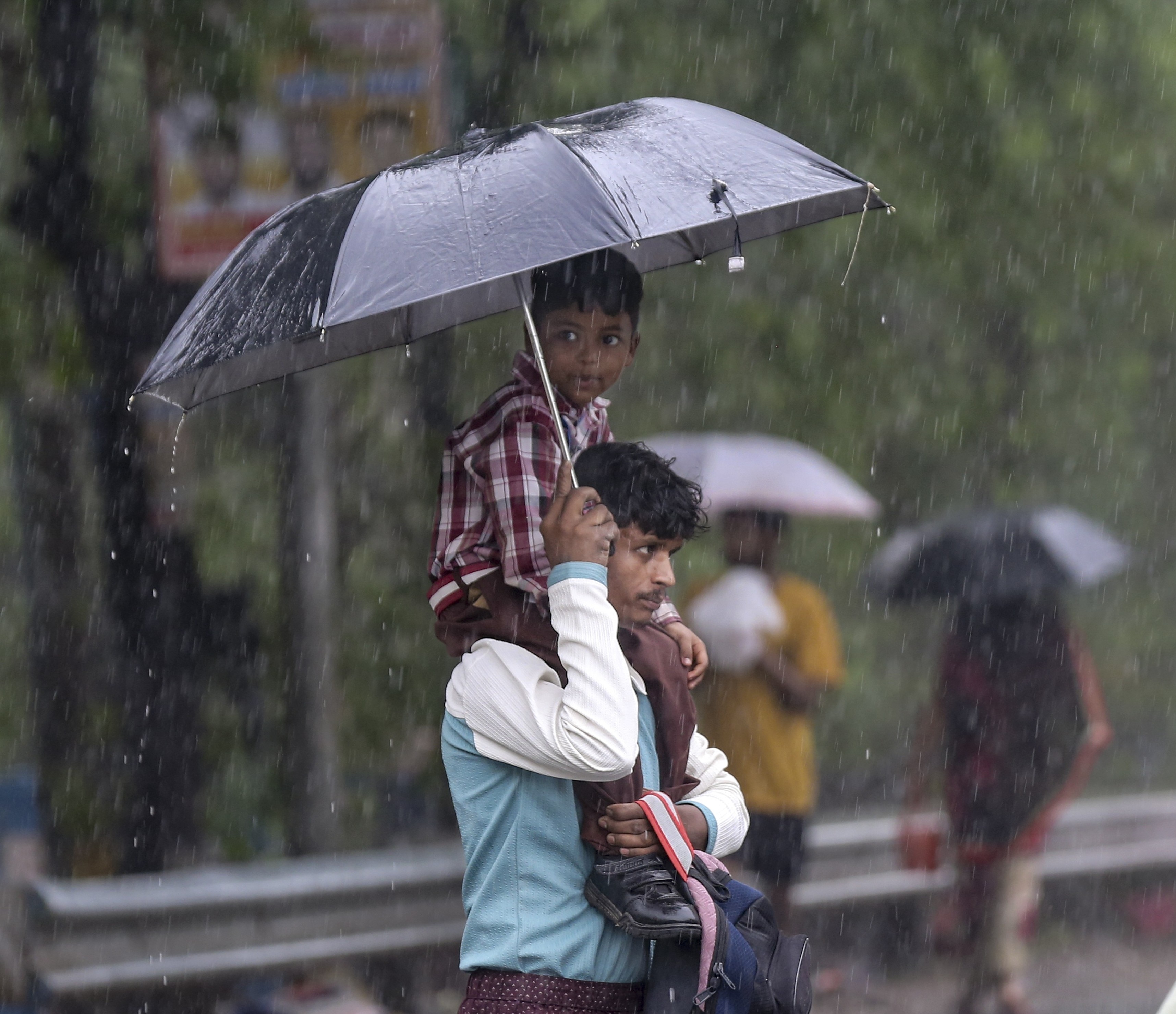 A man and his son take cover during the ongoing heavy rain in New Delhi. (Photo: PTI)