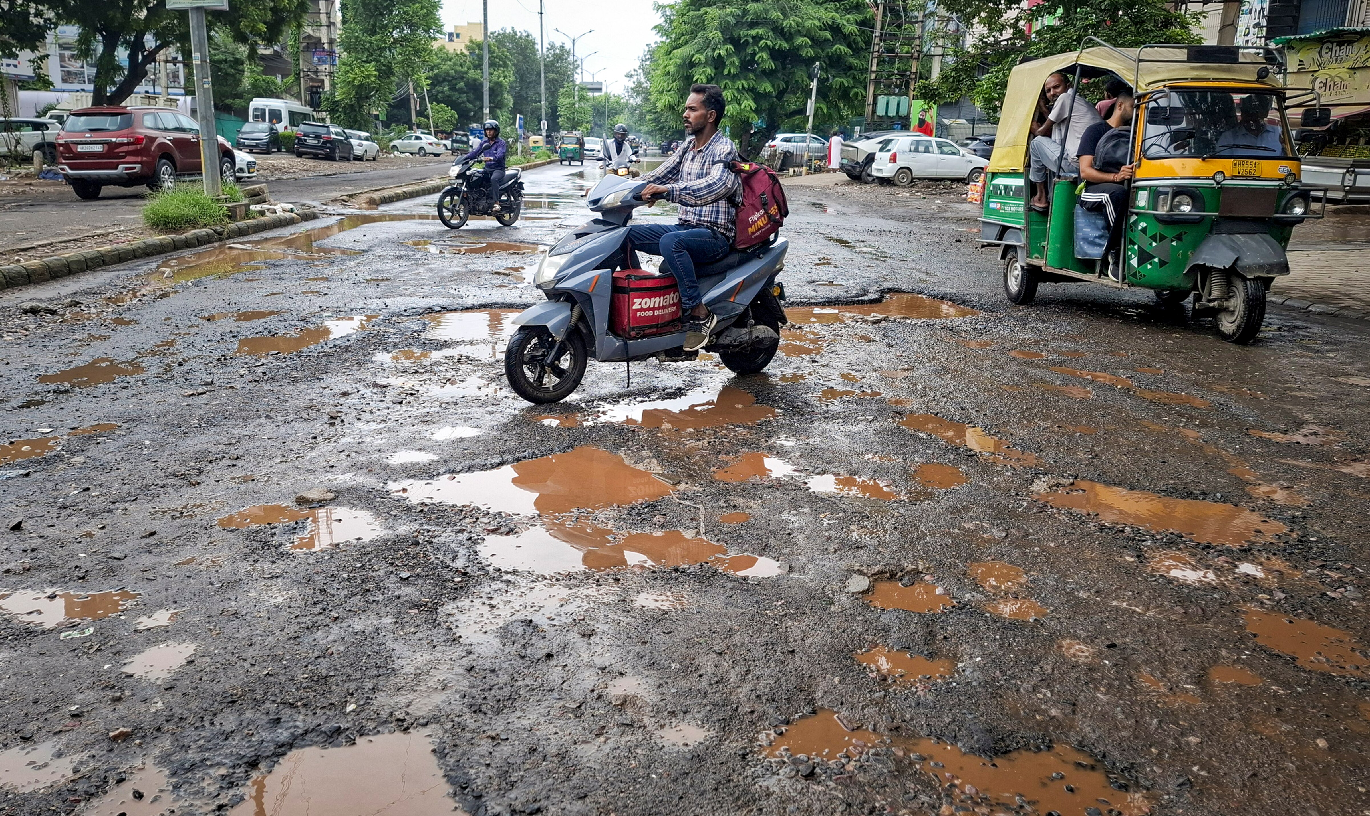 Commuters make their way through a pothole-ridden road after rain, in Gurugram. (Photo: PTI)