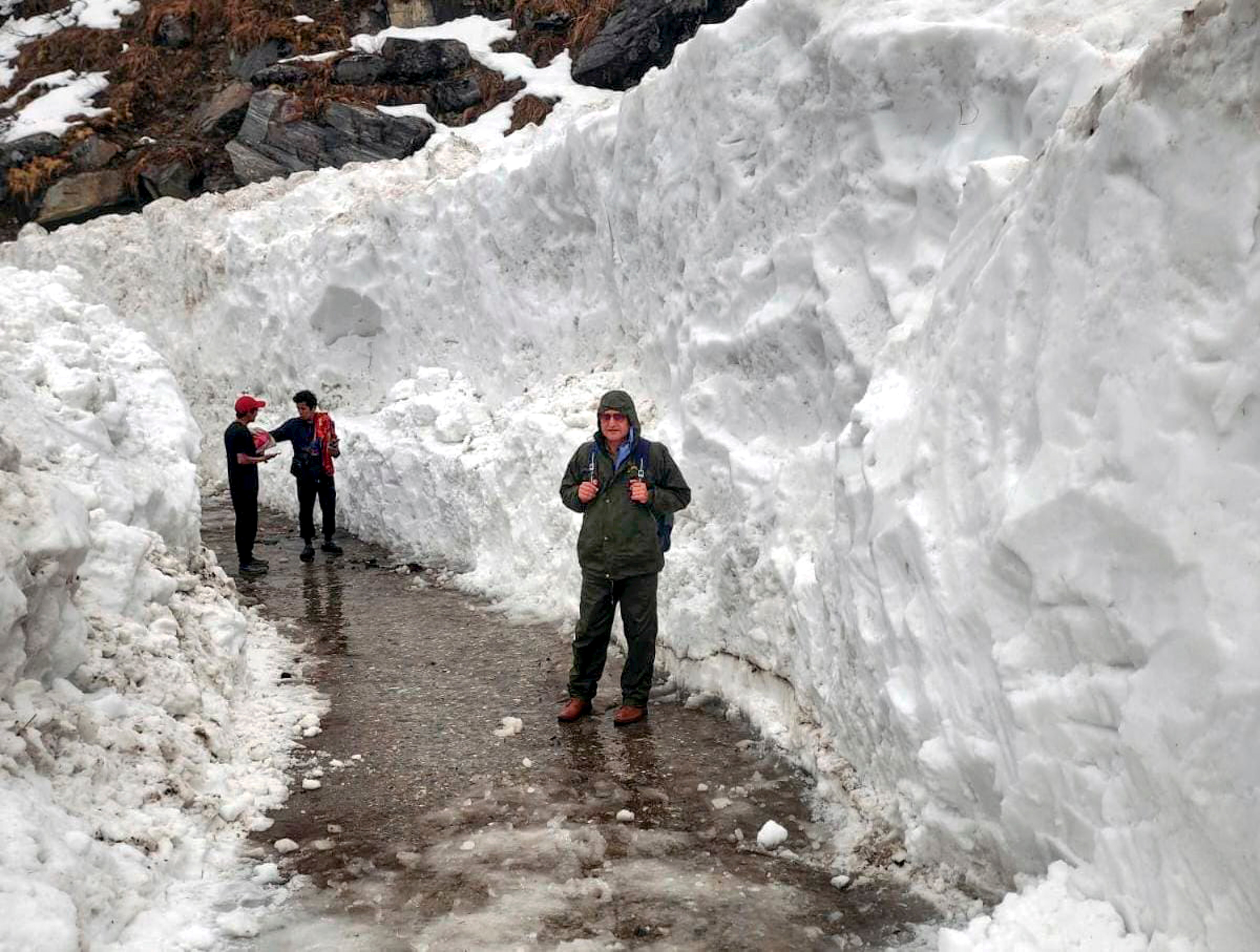 People walk along a snow-cleared path amid heavy accumulation following fresh snowfall near Kedarnath Dham. (Photo: PTI)
