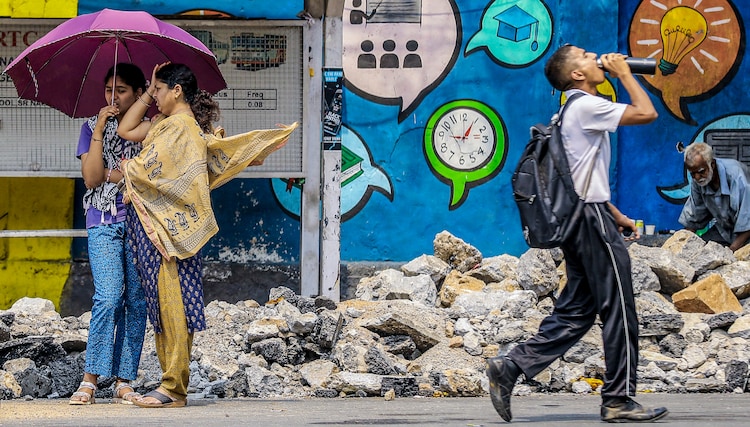 People use an umbrella and drink water to cope with the heat on a summer day. (Photo: PTI)