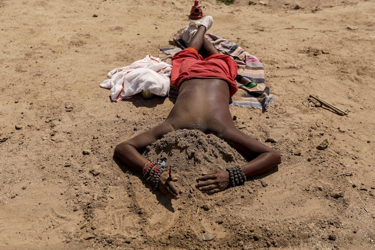 A man covers his head with sand to keep cool on a hot summer day at the Sangam. (Photo: PTI)