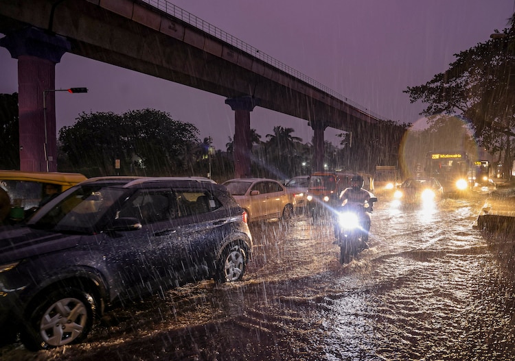 Commuters wade through a waterlogged road as rain lashes the city. (Photo: PTI)